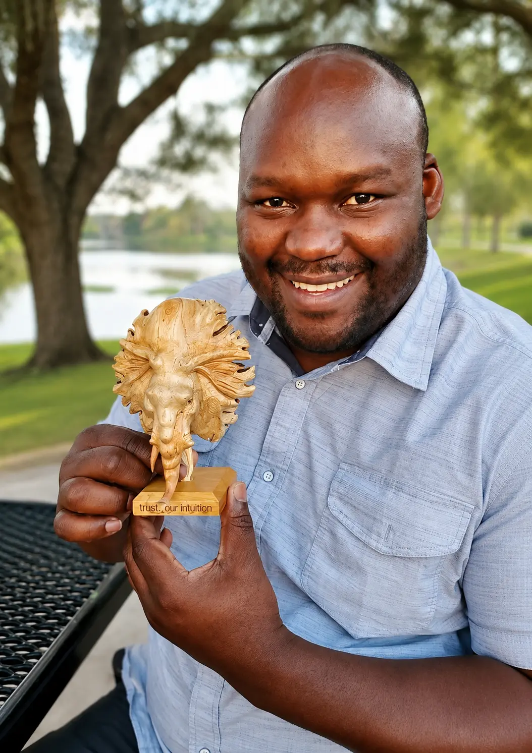 Patrick O. Odoyo smiling outdoors and holding a carved lion sculpture